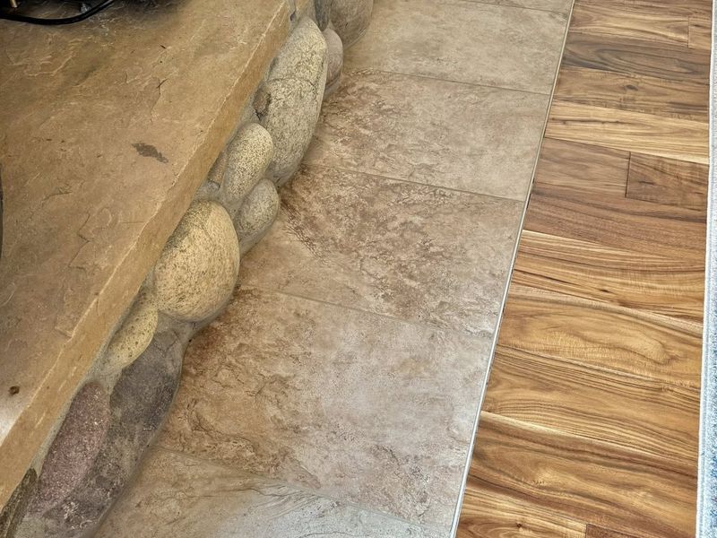 New tile hearth pad set into the hardwood at the river-rock wood stove