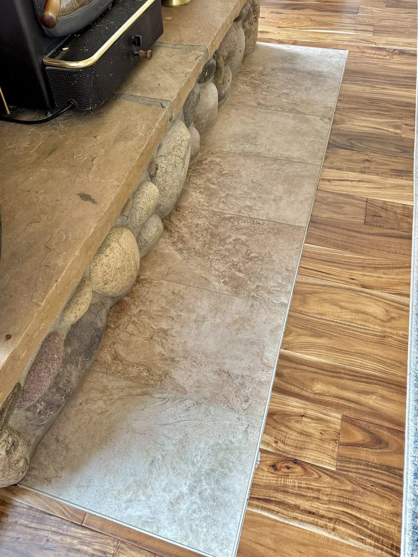 New tile hearth pad set into the hardwood at the river-rock wood stove