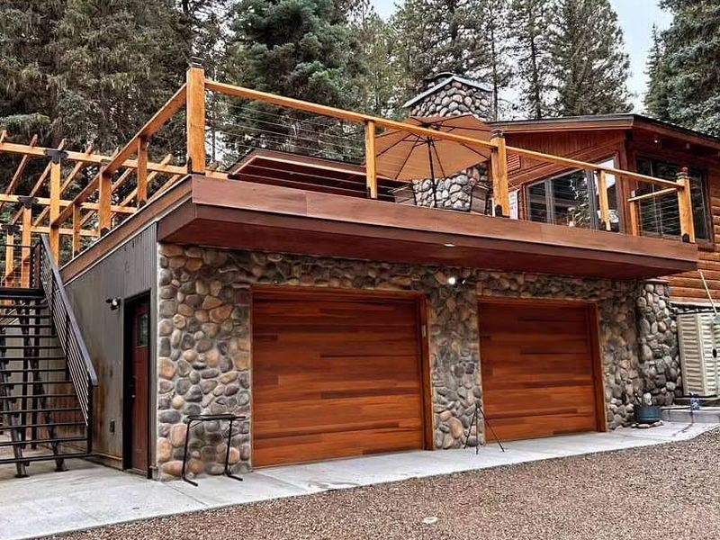 The finished garage: river-rock facing, cedar garage doors and a cable-rail deck above