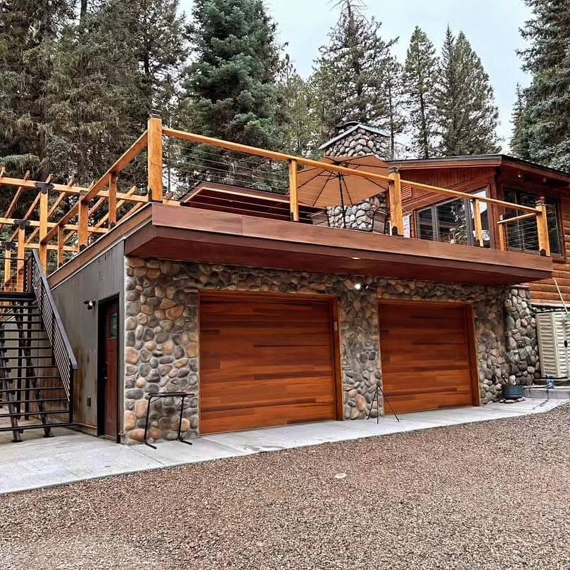 The finished garage: river-rock facing, cedar garage doors and a cable-rail deck above