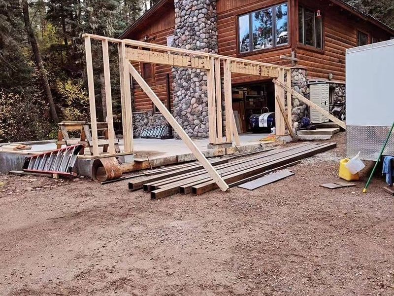New garage walls being framed on the slab beside the log home and river-rock chimney
