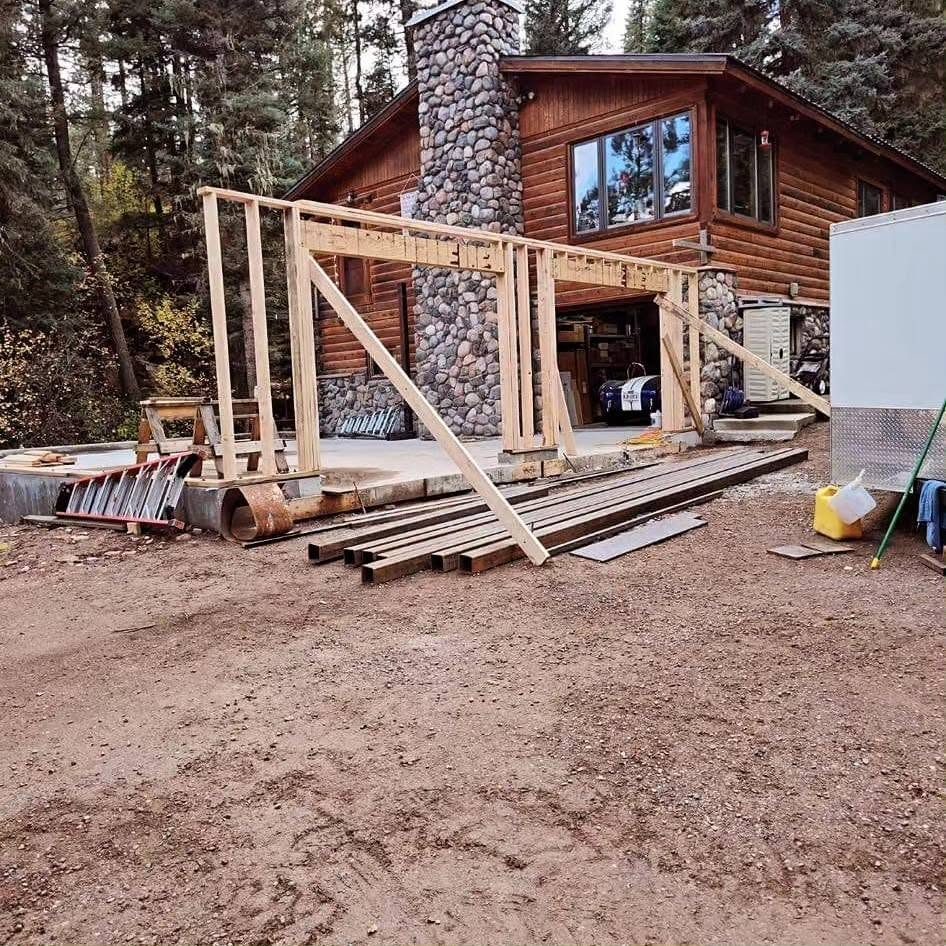 New garage walls being framed on the slab beside the log home and river-rock chimney