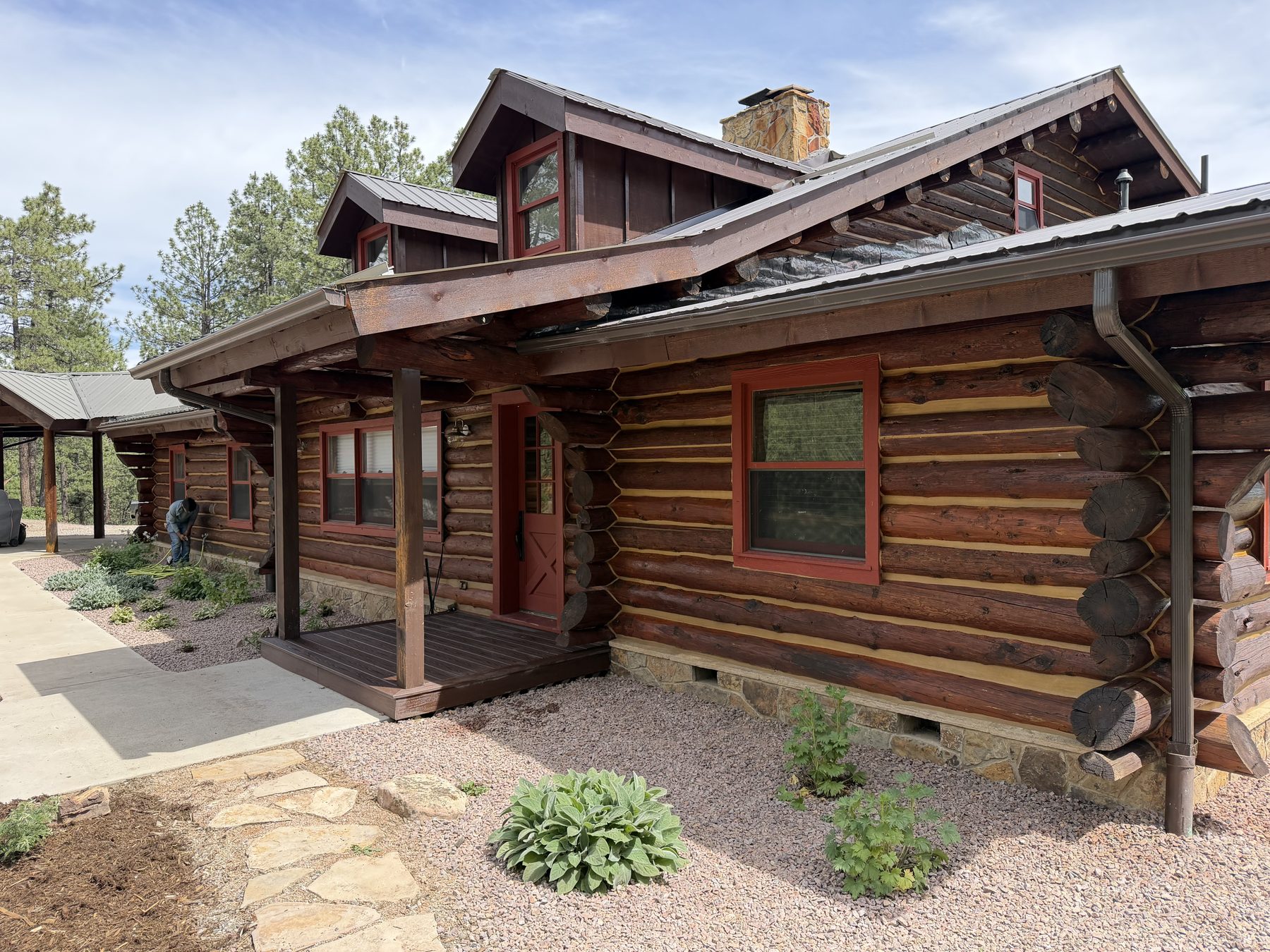 A log home with freshly stained logs, red window trim and a covered porch